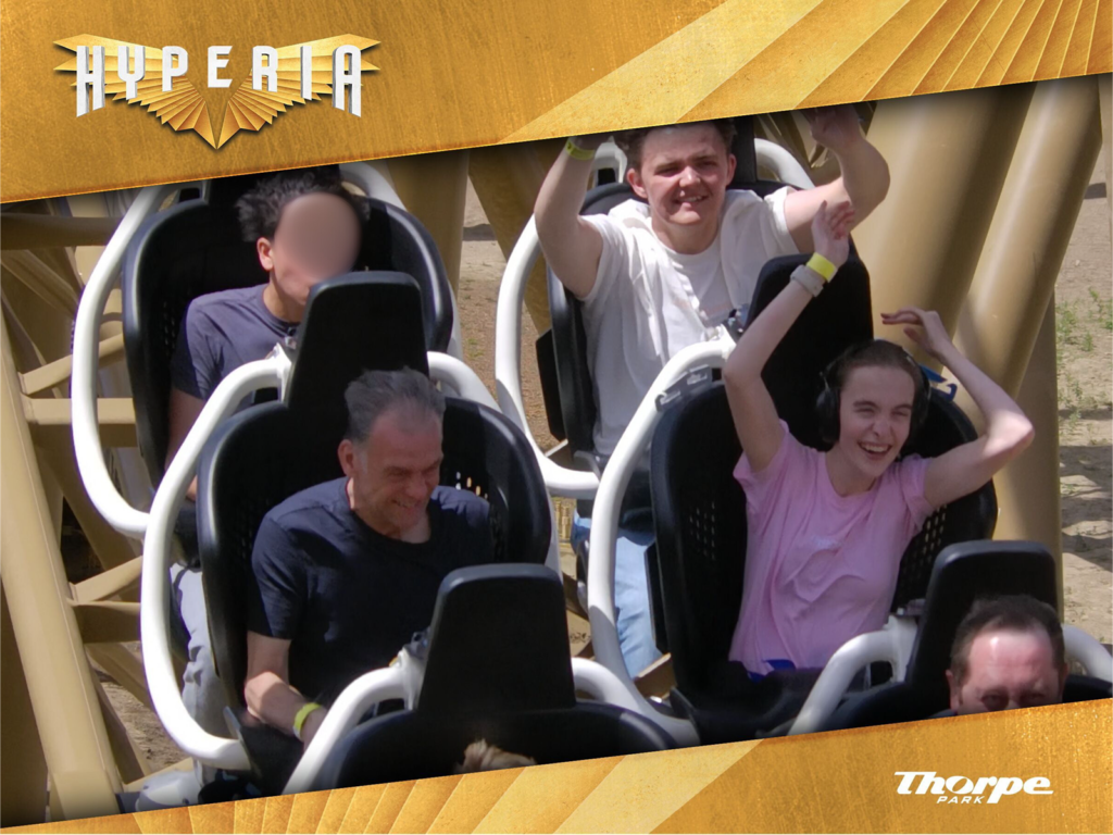 Image shows Iona and Dad on ride photo for Hyperia. Iona has her hands in the air and is smiling