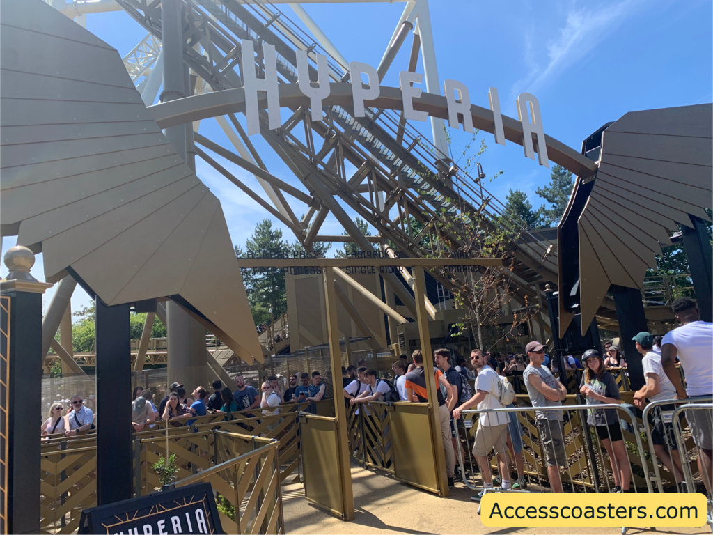 Image of Hyperia queue line in the image you can see two big gold wings as the entrance portal for the queue line the queue line from  left to right are ride access pass and step free access, FastTrack and single rider, main queue line   