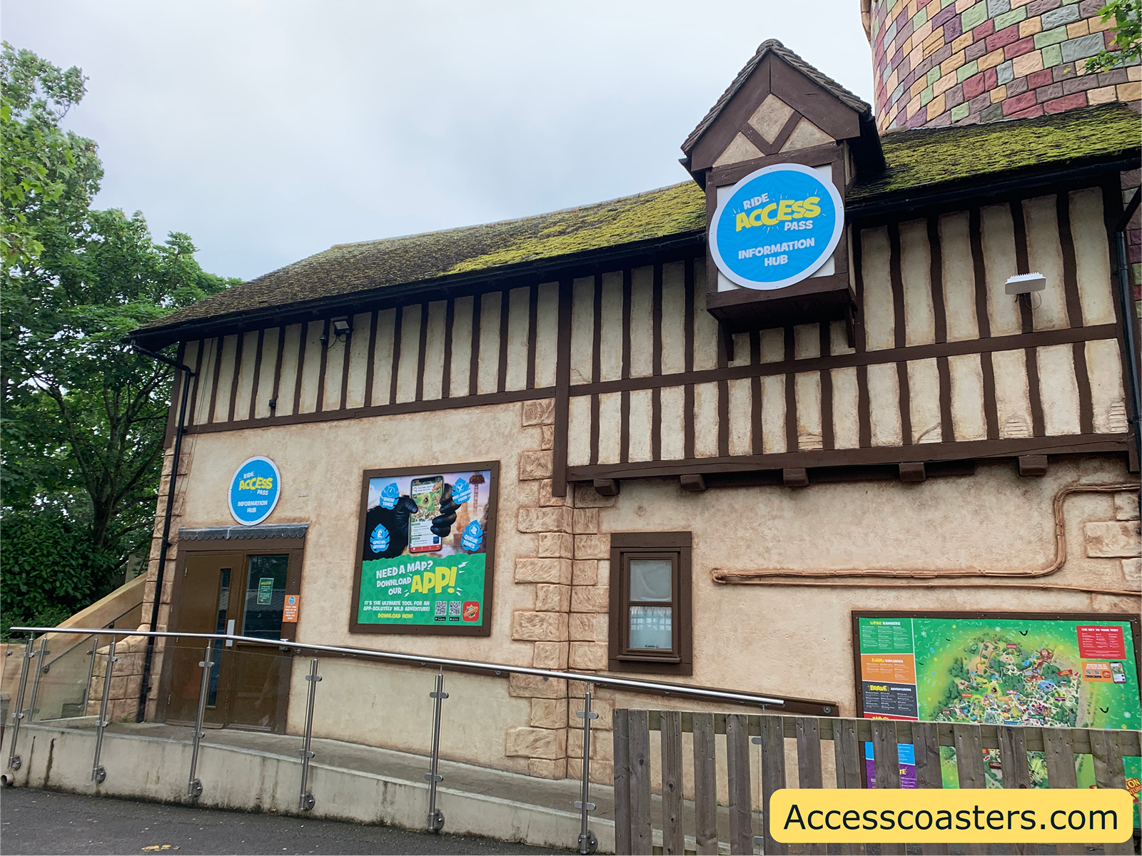 Image of Chessington rode access pass hub entrance. In the image you can see a long ramp leading up to the door with a large map of the park on the side of the building as well as a sign on top of the building saying ride access pass hub.