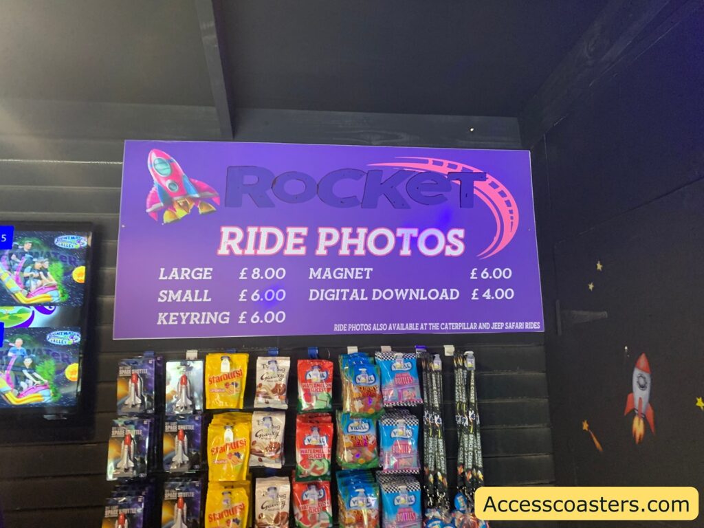 image shows a sign with the ride prices for the rocket roller-coaster ride phots. the sign reads large £8, small £6, keyring £6, magnet £6, digital download £4. 