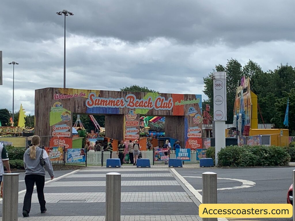 image shows the entrance to summer beach club from across the road. in the image you can see some rides in the background as well as a big sign saying summer beach club. 