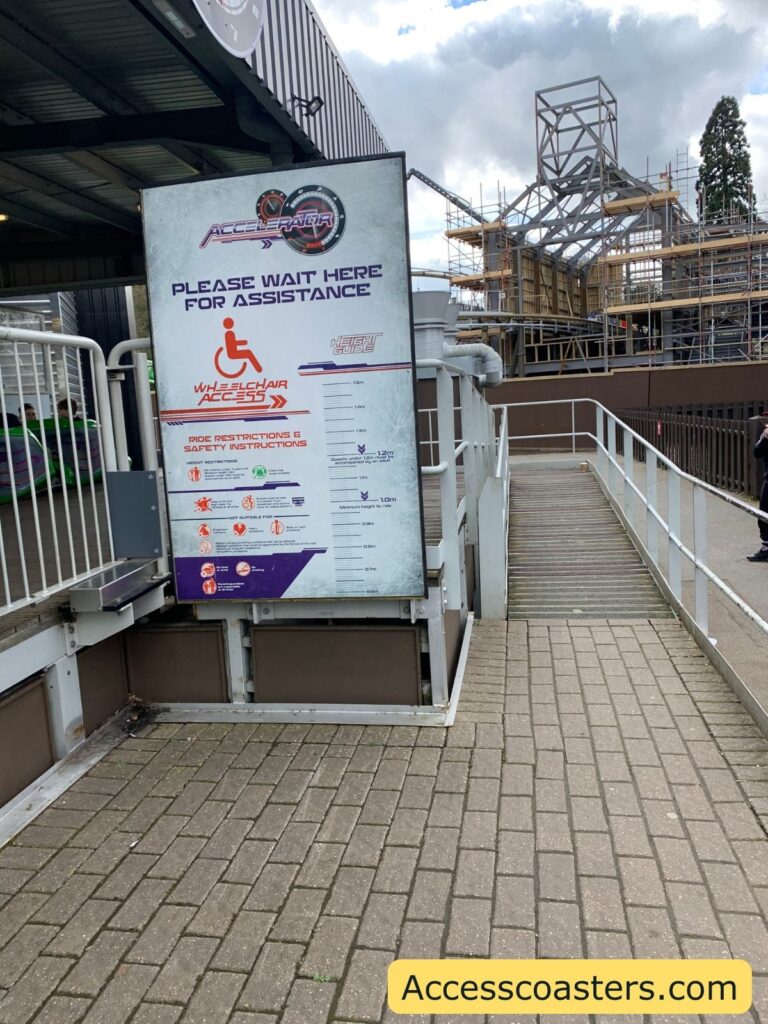 In the image you can see a ramp leading up to in the image you can see a door leading through to a queueline with a sign to the ride station with a sign saying wheelchair access 