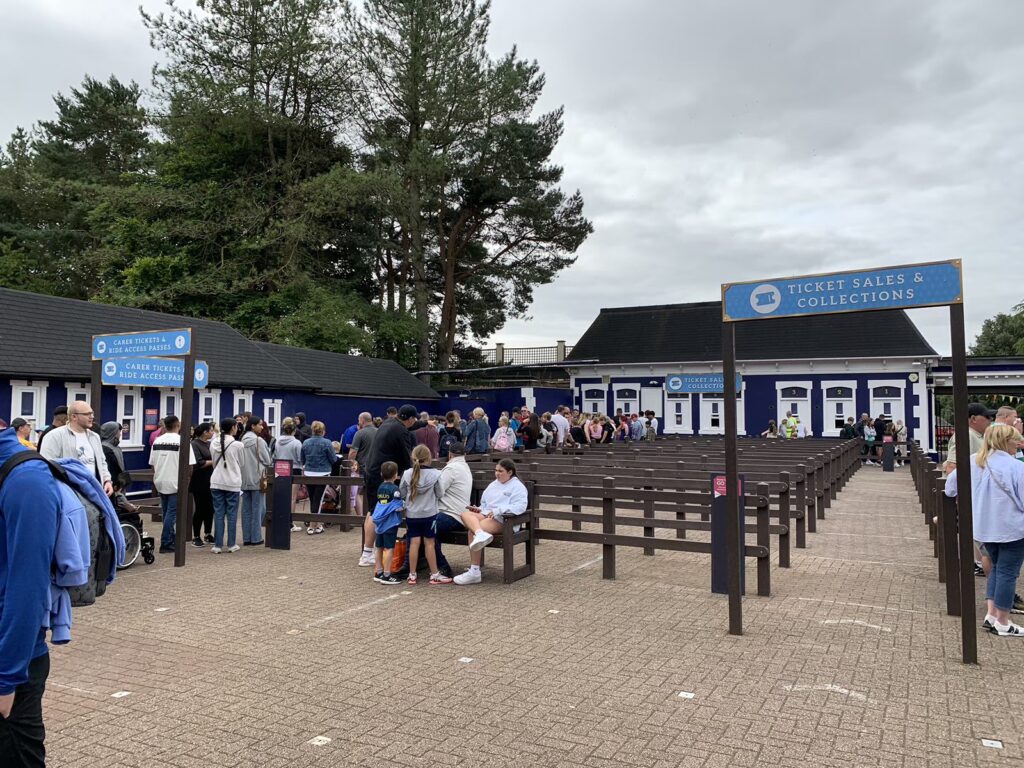 Image shows two queue lines leading up to kiosk windows. one queue has a sign says ticket office and the other says carer tickets and ride access pass.