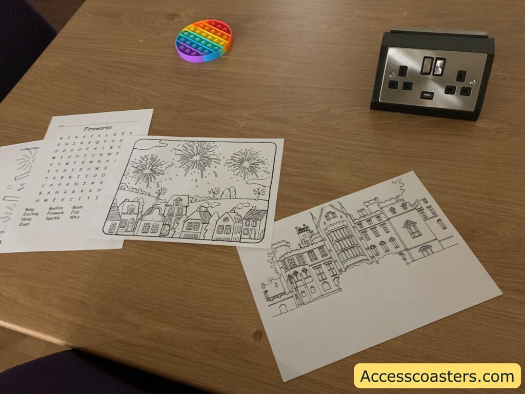 image shows a table with a charging plug, alton towers colouring sheets fireworks worksheet and a pop it.