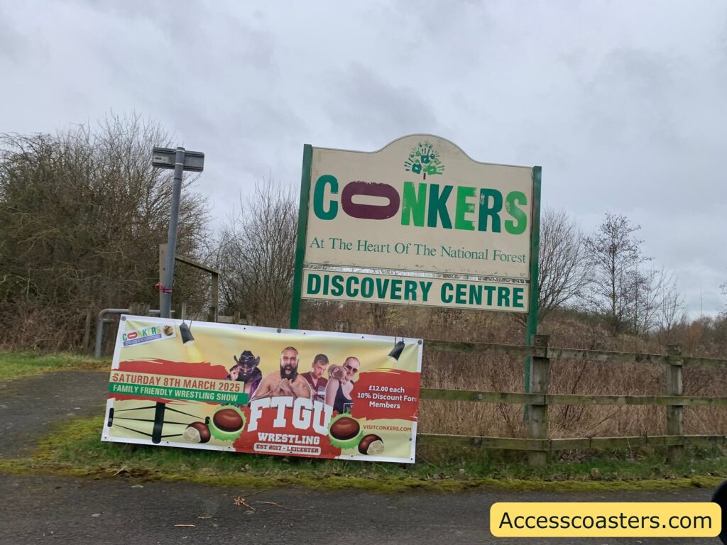 Sign for "CONKERS" at the Heart of the National Forest, Discovery Centre. Below it, a banner advertises a family-friendly wrestling show on Saturday, 8th March 2025, featuring "FTGU Wrestling" established in 2017 in Leicester. The banner includes images of wrestlers and states tickets are £12.00 each with a 10% discount for members. The website mentioned is visitconkers.com. The surrounding area has leafless trees and a cloudy sky.
