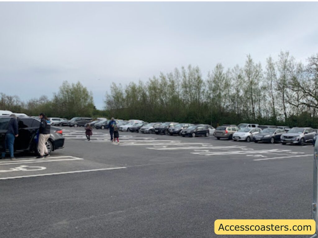 The image shows a large, open parking lot with many cars parked in rows. In the foreground, there are two people standing next to a dark-colored car