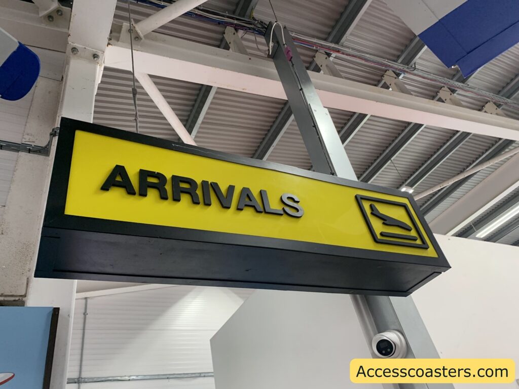 Airport arrivals sign. The image shows a rectangular yellow and black sign hanging from the ceiling. The sign has the word "ARRIVALS" in bold black letters on the left, and on the right, there is a pictogram of an airplane landing.