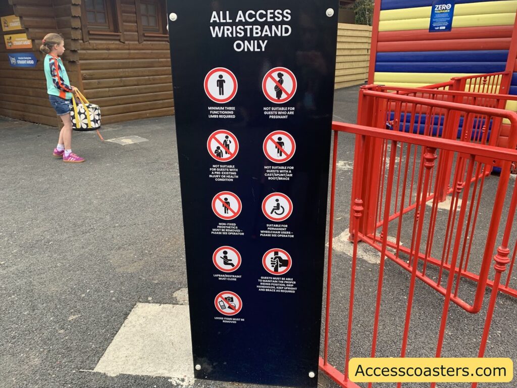 Black signboard with white text and red prohibition symbols, located at the entrance to an amusement attraction. The sign reads "ALL ACCESS WRISTBAND ONLY" at the top, followed by a series of circular icons with red slashes indicating restrictions. The rules listed are:

- Minimum three functioning limbs required
- Not suitable for guests who are pregnant
- Not suitable for guests with a prosthesis, injury, or health condition
- Not suitable for guests with a cast, splint, air boot, or brace
- Non-fixed upper/lower limb prosthesis—please see operator
- Suitable for permanent wheelchairs—please see operator
- Lapbar/restraint must close
- Loose items must be removed
- Guests must be able to support head and body without aid, keep upright, and remove splint or brace as required