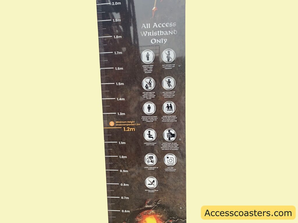 Height measurement board with safety and access instructions. The board is marked with height measurements from 0.6 meters up to 2.0 meters. There is a highlighted line at 1.2 meters, labeled "Minimum Height Unaccompanied 1.2m."

To the right of the height scale, there are several circular icons with text, indicating rules and restrictions. Some of the visible instructions include:
- All Access Wristband Only
- Not suitable for pregnant women
- Not suitable for guests with heart conditions
- Not suitable for guests with back or neck problems
- Wheelchair users must be able to transfer with assistance
- Loose items must be secured
- No food or drink
- No photography