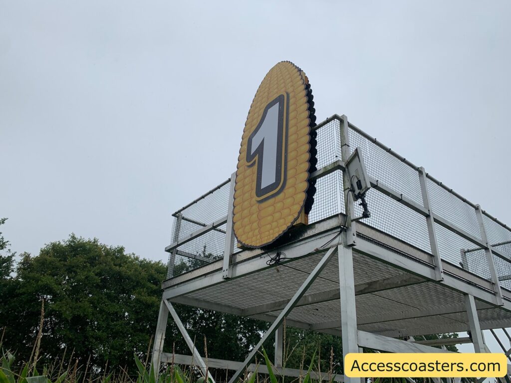 Metal platform structure with a large yellow sign shaped like an ear of corn, featuring a bold black and white number "1" in the center. The platform is surrounded by metal mesh railings, 