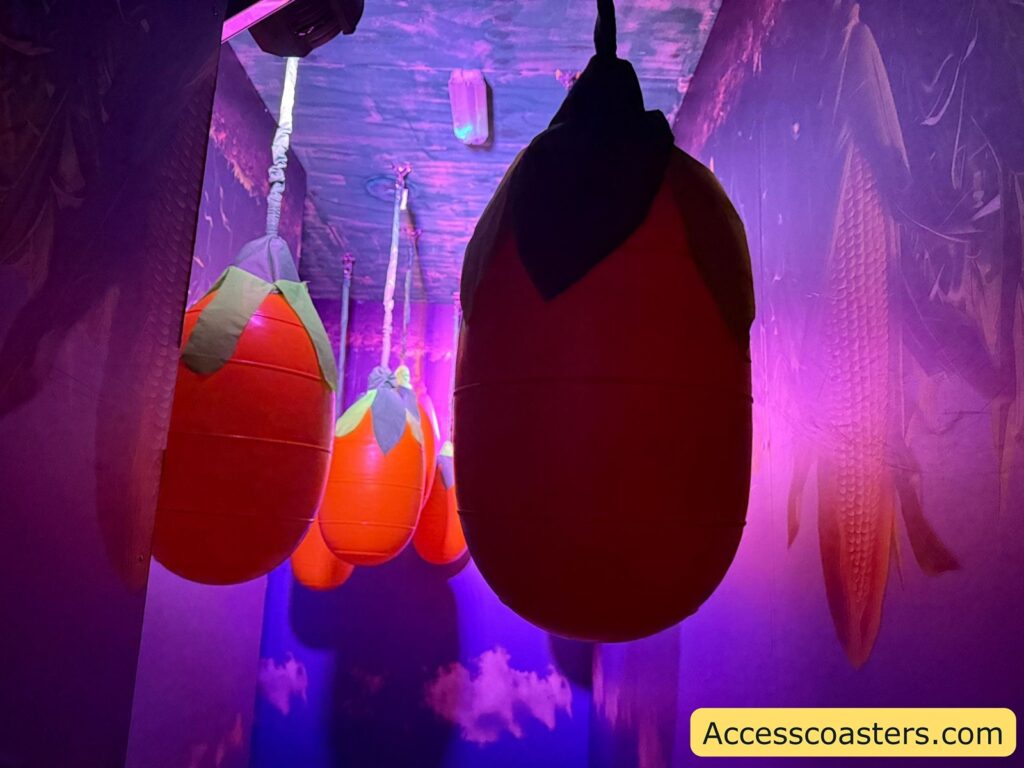 Large, hanging fruit-shaped objects in a dimly lit hallway. The objects resemble oversized strawberries or tomatoes, with red bodies and green tops, suspended from the ceiling by ropes. 
