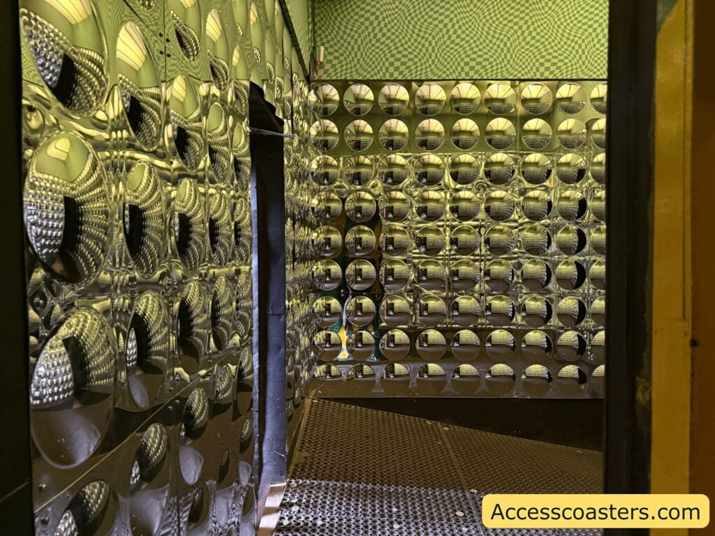 Metallic, reflective room with circular, concave patterns covering the walls. The surfaces create a distorted, almost funhouse mirror effect. The floor appears to be made of metal grating, and the ceiling has a green and white checkered pattern.