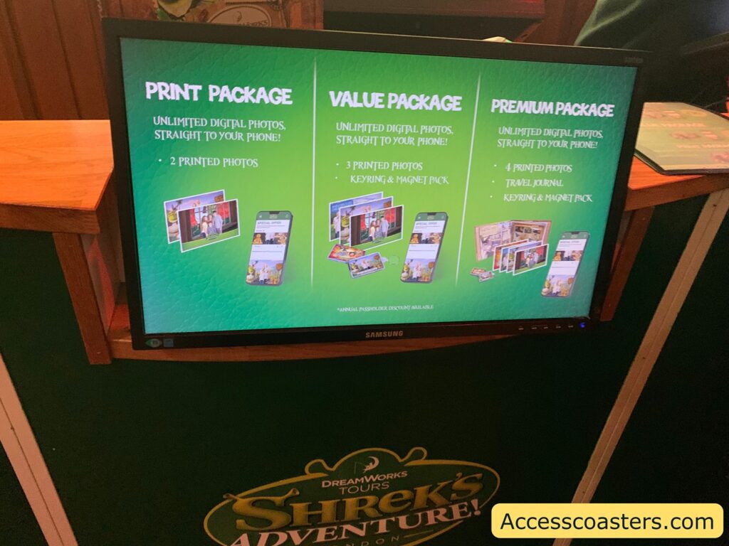 A digital display screen showing three photo package options for DreamWorks Tours Shrek's Adventure. The background is green, and the packages are listed from left to right:

Print Package:
Unlimited digital photos, straight to your phone!
2 printed photos

Value Package:
Unlimited digital photos, straight to your phone!
3 printed photos
Keyring & magnet pack

Premium Package:
Unlimited digital photos, straight to your phone!
4 printed photos
Travel journal
Keyring & magnet pack

There are small images below each package showing examples of printed photos, a phone, and the included items. At the bottom of the screen, there is a note: *Annual passholder discount available.