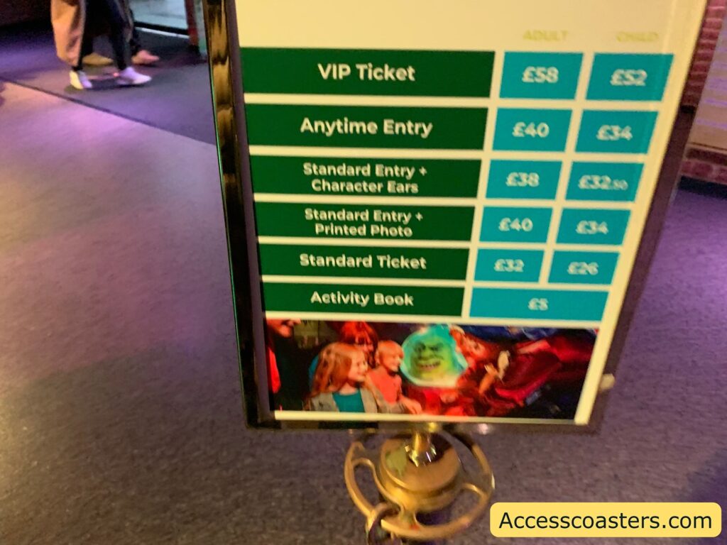 A price board for tickets and extras at an attraction. The board is divided into categories for adults and children, with prices listed in British pounds. The options are:

VIP Ticket: Adult £58, Child £52
Anytime Entry: Adult £40, Child £34
Standard Entry + Character Ears: Adult £38, Child £32.50
Standard Entry + Printed Photo: Adult £40, Child £34
Standard Ticket: Adult £32, Child £26
Activity Book: £5