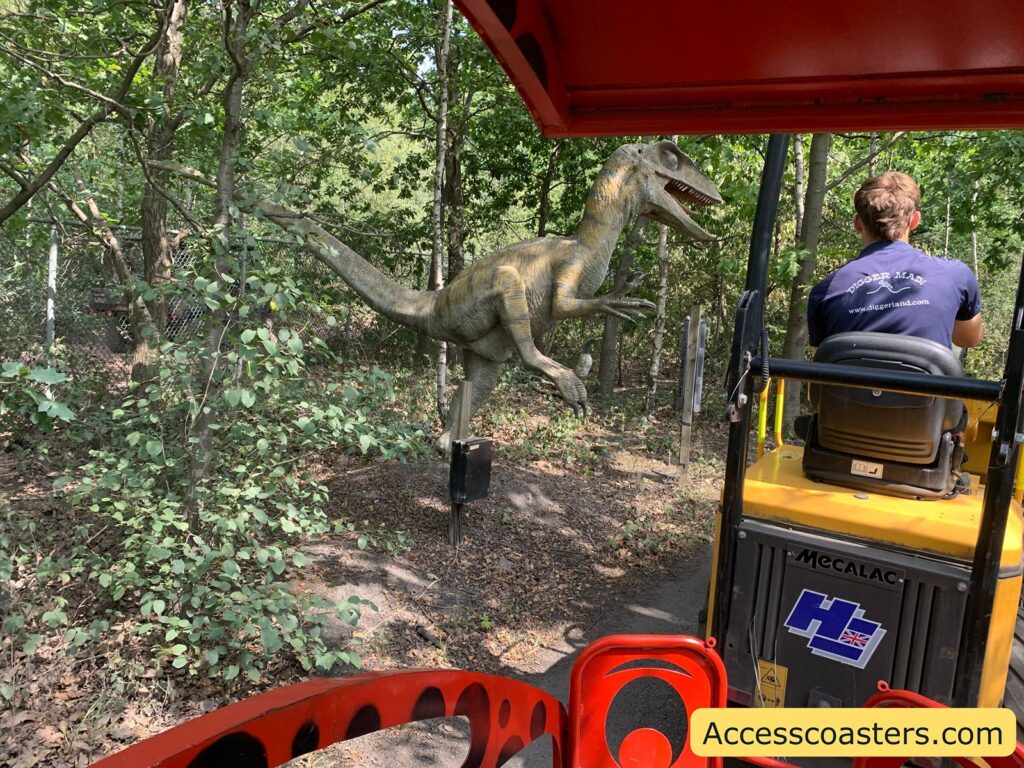 Dinosaur model in a wooded area, seen from the perspective of the train ride