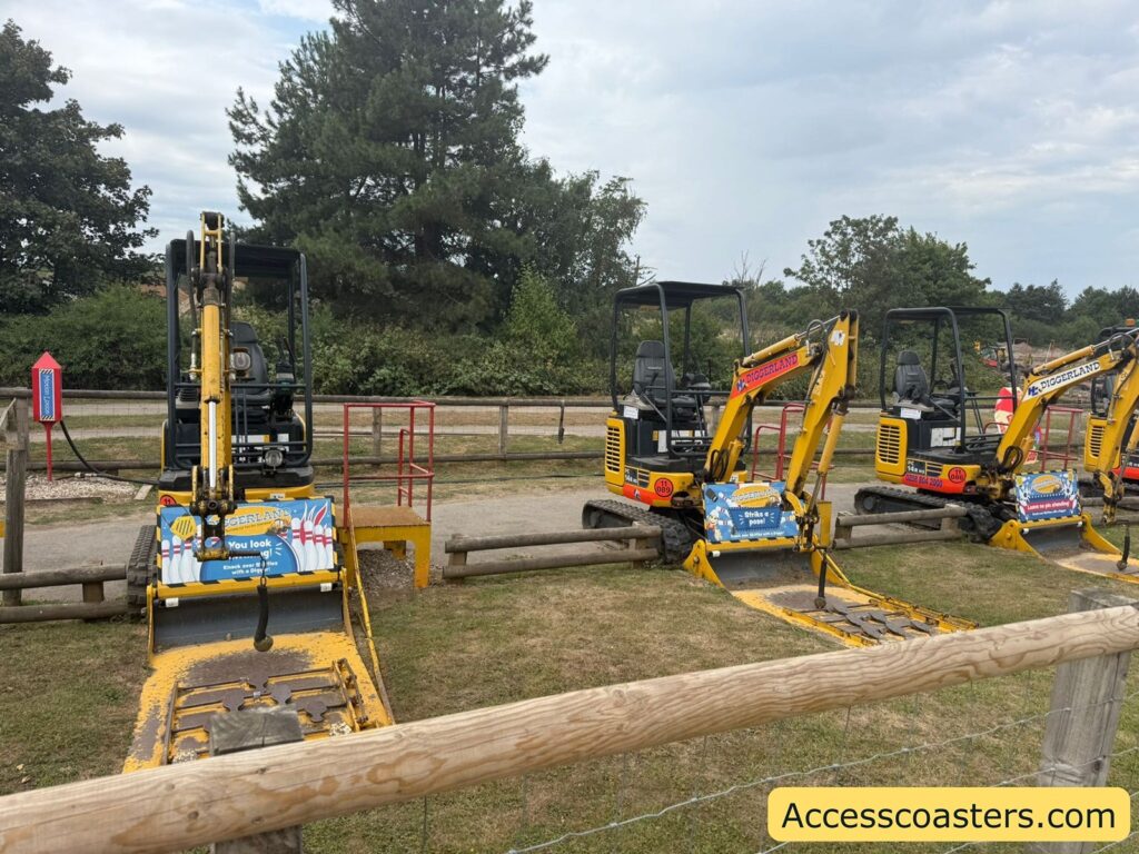 Row of small yellow excavators lined up on grass, each with a blue and yellow Diggerland sign attached to the front. each digger has a ball on some string attrached with some bowling skitlles on the floor