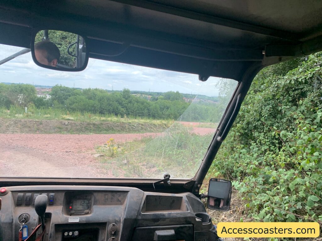 View from inside an off-road vehicle, showing a dusty dashboard with a small screen, various buttons, a steering wheel and a dirt track