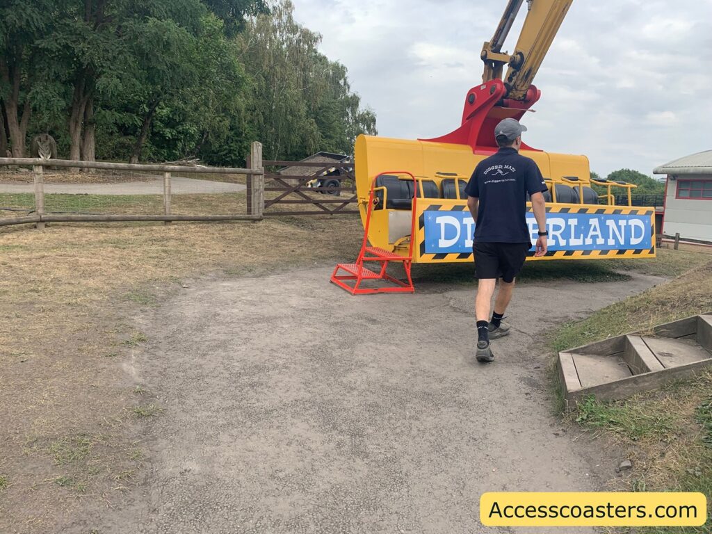 walking towards a bright yellow amusement ride vehicle. The vehicle has a blue and white sign on the front that reads "DIGGERLAND." The ride looks like it is based on construction equipment, 2 red steps up to the ride vhacal is visable