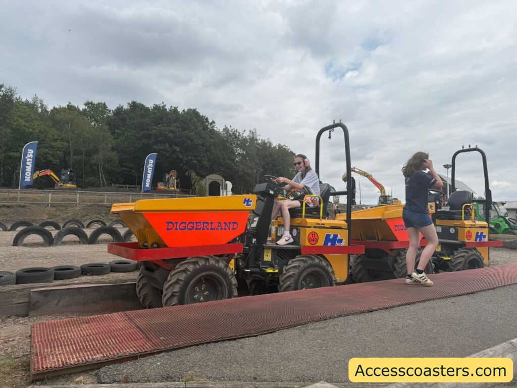 brightly colored yellow and orange construction vehicle, labeled "DIGGERLAND" in blue and red letters. Iona wearing pink earmuffs and sunglasses is sitting at the driver’s seat of the vehicle, smiling.