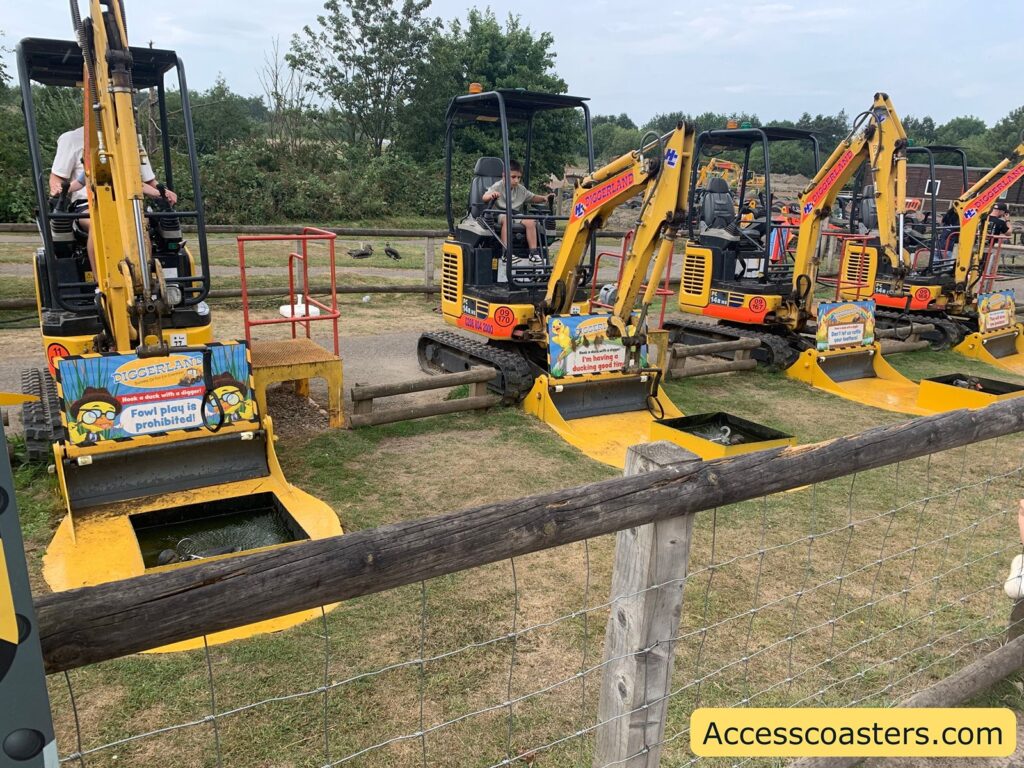 Row of small yellow diggers at a children's amusement attraction, each equipped with a sign on the front. The diggers are set up next to small water-filled pits