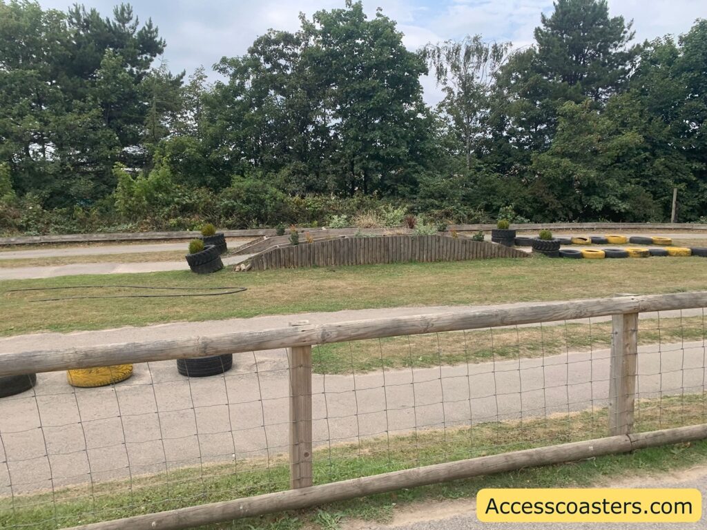 track bordered by wooden fencing. The track is made up of a paved path with several yellow and black tires used as barriers along the edges and at a small central island area