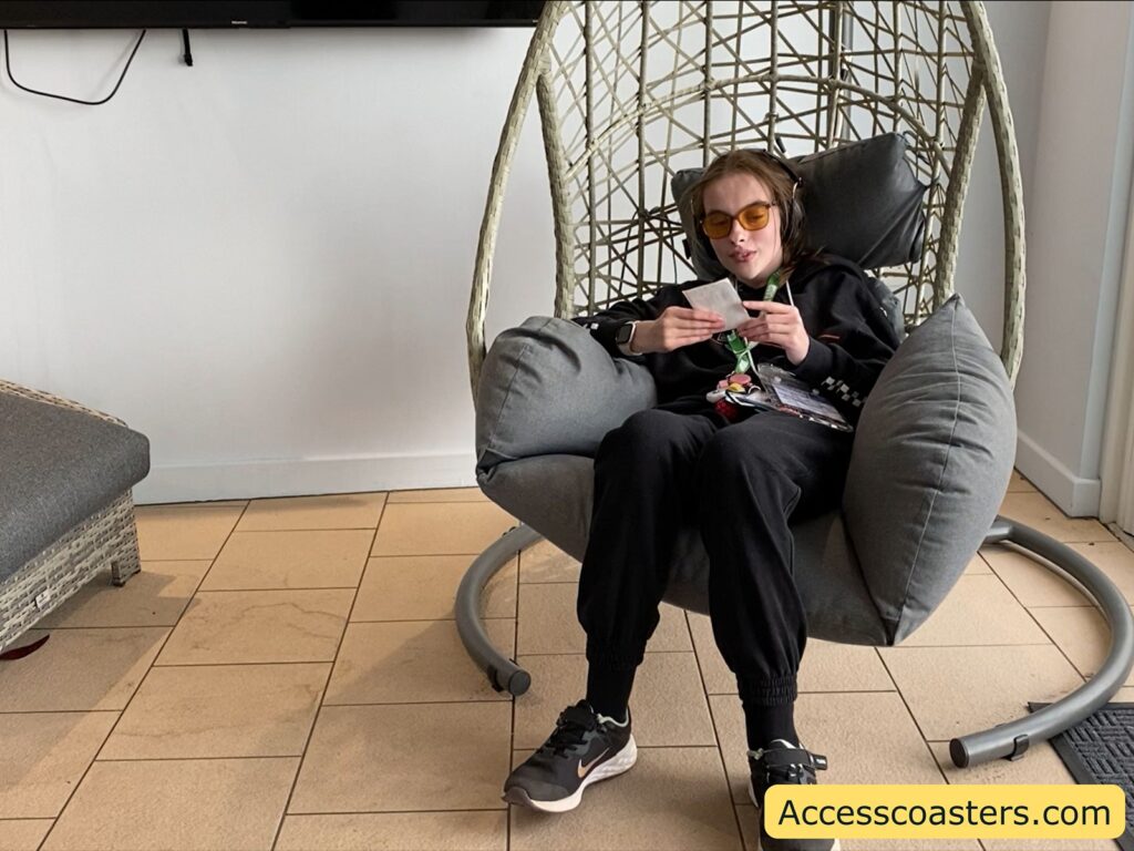Iona relaxing in a large hanging egg chair inside Thorpe Park’s quiet room, using a mobile phone.