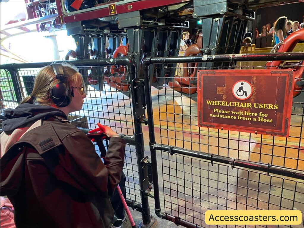 Person using a cane waiting in the ride station next to a sign giving instructions for wheelchair users at Nemesis Inferno.