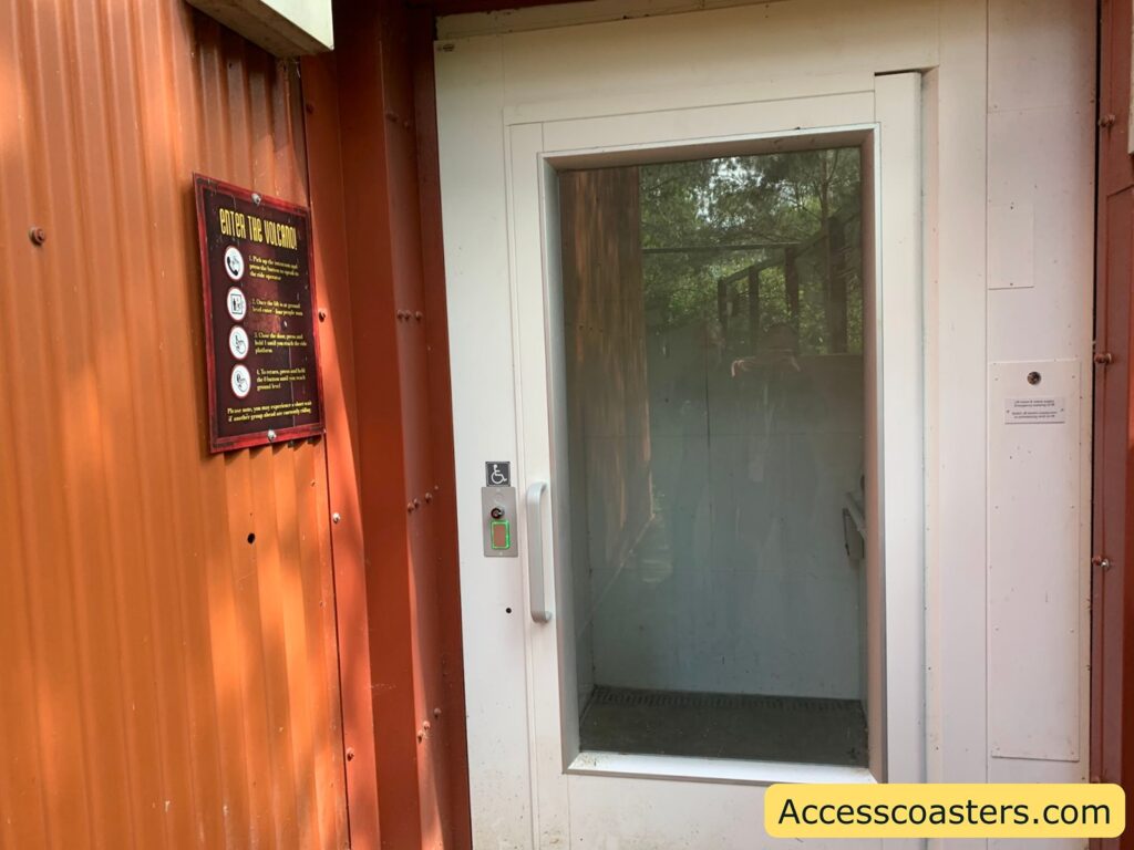 Close-up of a white accessible lift entrance at Nemesis Inferno, with information signs visible on the orange wall.