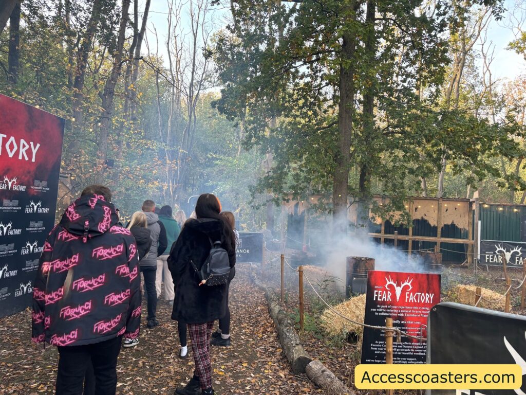 Queue of visitors waiting outside in a wooded area, with some fog or smoke adding to the spooky atmosphere.