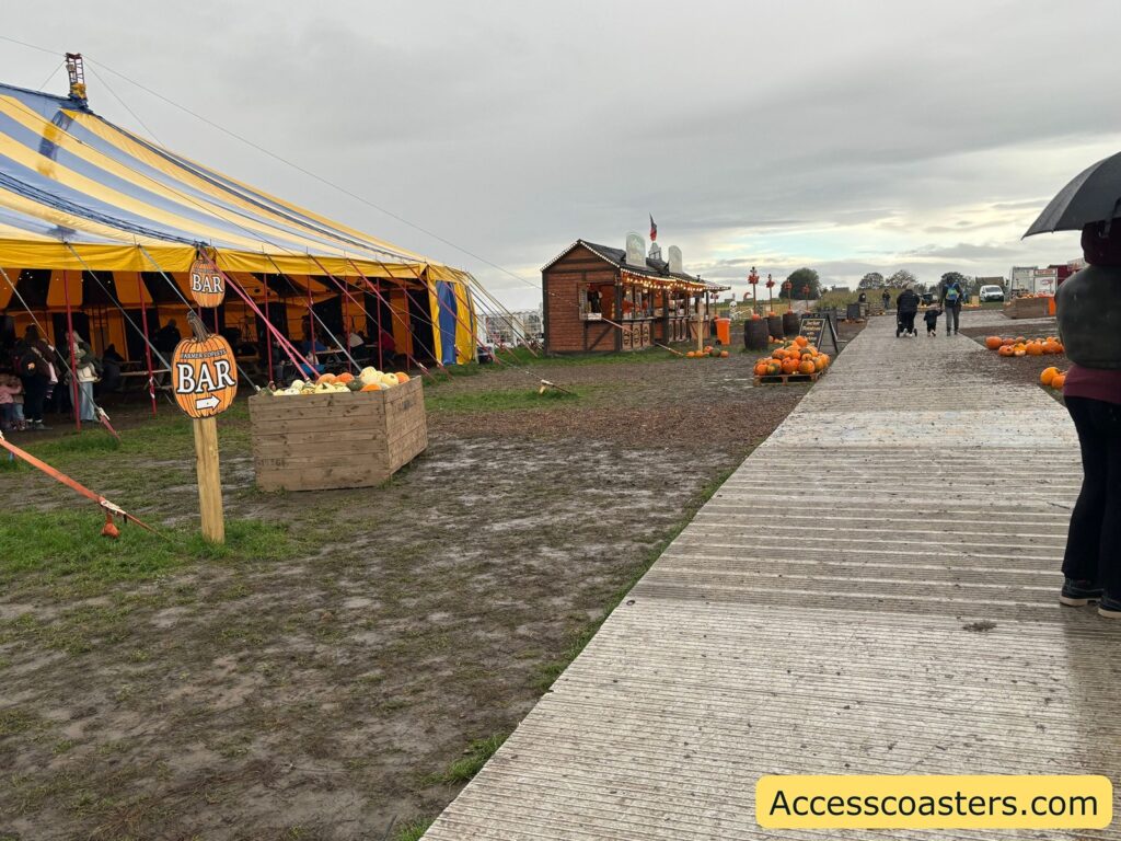 Photo of a boardwalk-style path laid over grass at an outdoor festival, with food stalls, picnic tables, and people along the walkway 