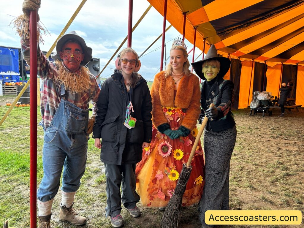 : Three people posing in front of the marquee, one dressed as a scarecrow, one as a witch, and another in a flower-themed costume.