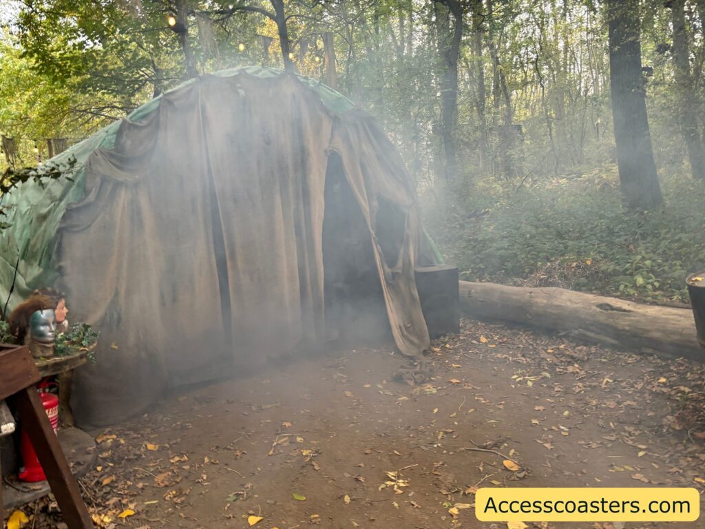 The exterior of a scare zone tunnel covered in weathered tarps, surrounded by woodland. A misty, smoky effect 