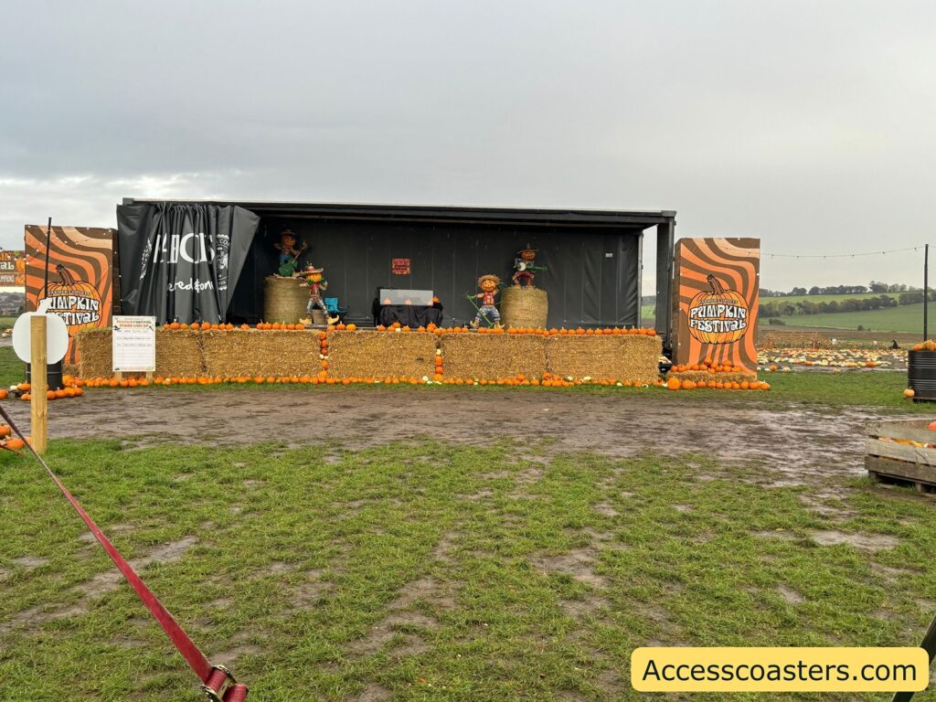 A wide, clear view of the festival stage decorated with hay bales and pumpkins, set in an open field,