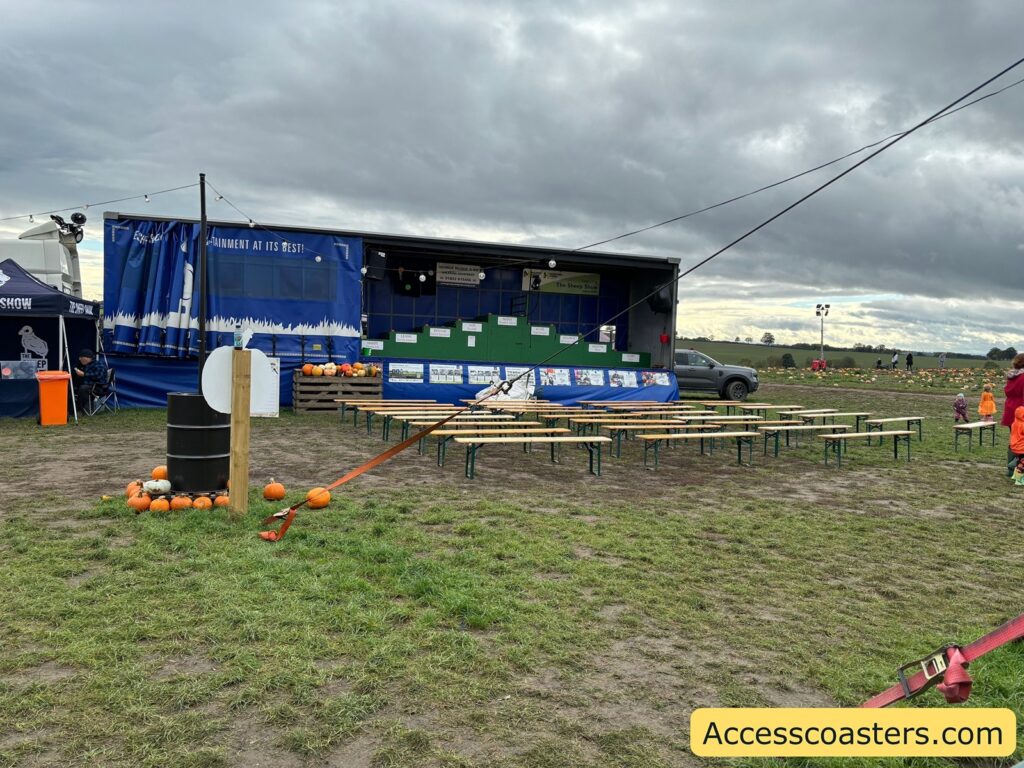 A wide view of the sheep show setup, showing the blue stage, benches, grassy field,