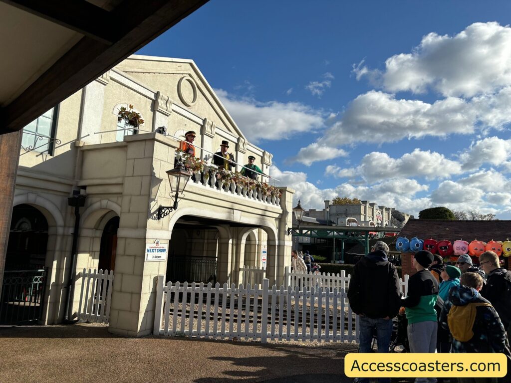 A wider view of the white Thomas Land building with people gathering in front and along the side, while a few characters appear on the balcony above. The area is busy with families enjoying the Halloween event