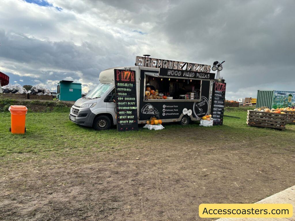  A rustic pizza van set up on grass at the pumpkin festival, with a menu board and picnic bench