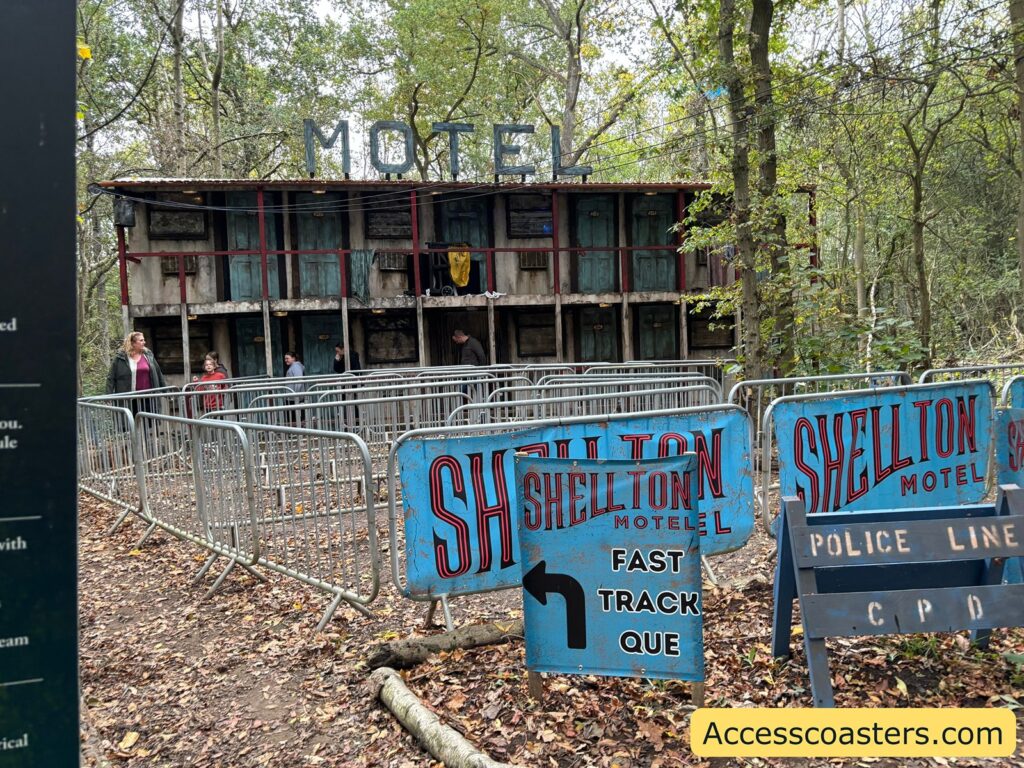Exterior view of the Shellton Motel attraction, showing a two-story, wooden building surrounded by trees. A blue police line sign is visible in front of the building with a fast track queueline 