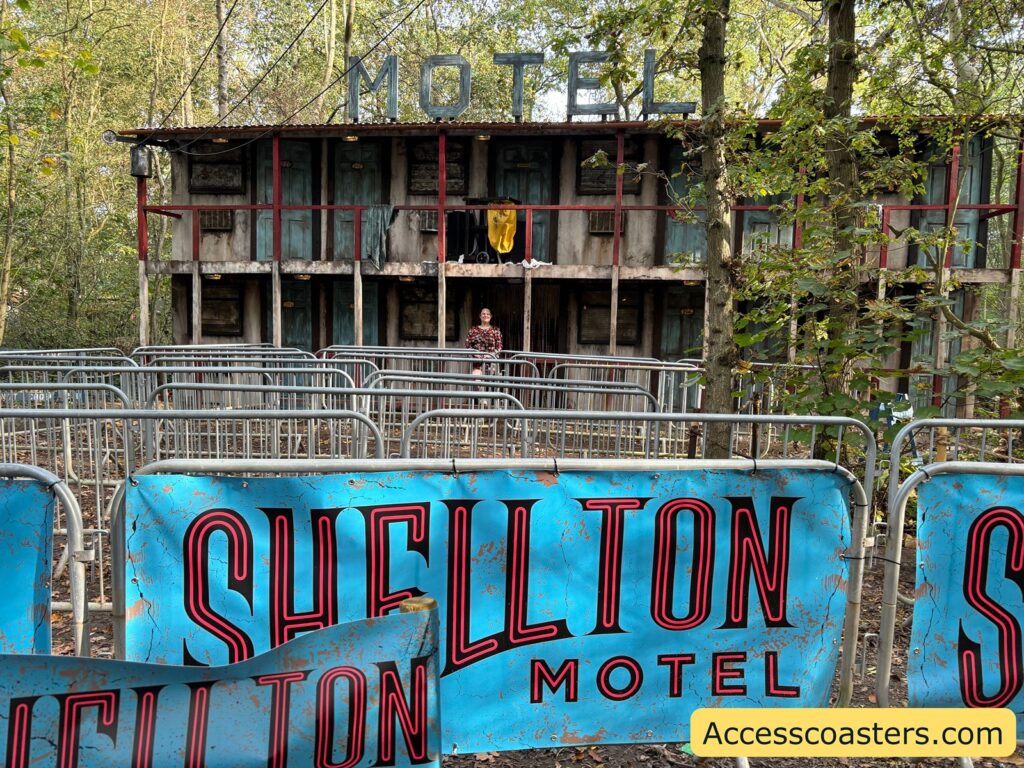 Front view of the Shellton Motel with a large, weathered sign reading 'Shellton Motel' and additional themed signage in a wooded outdoor setting.