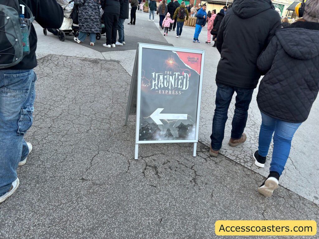 Entrance sign pointing towards the Haunted Express train ride with crowds walking nearby.