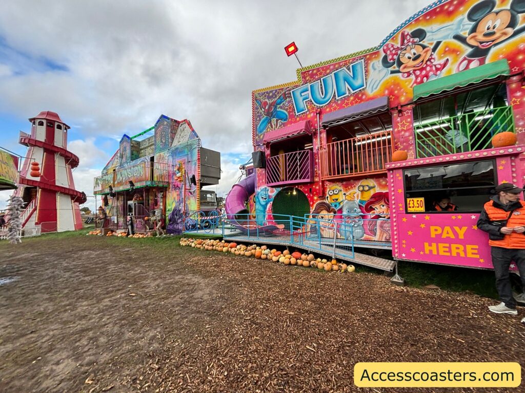 Close-up of a vividly painted fun house with “PAY HERE” sign, next to the red-and-white helter skelter.