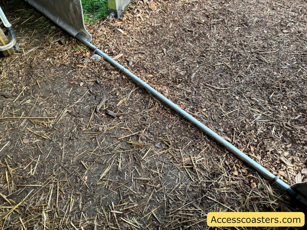  close-up view of a low metal bar on the ground at the tent entrance, marking a threshold between grass and wood chip flooring.