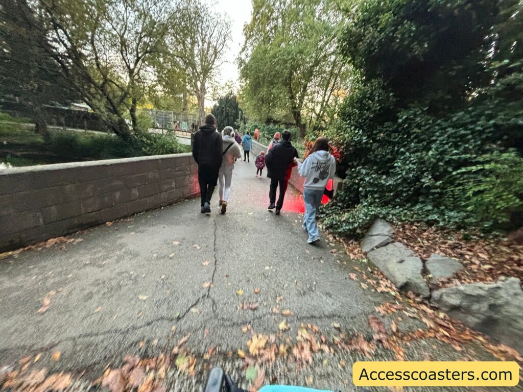 people, including a child, walking along a wide, accessible path with trees and bushes on either side.