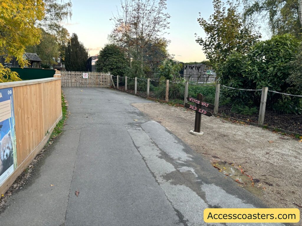 walkway edged by fences and greenery with halloween sign