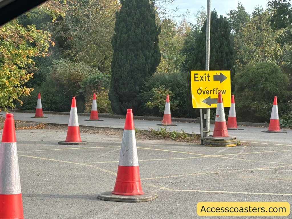 Event parking lot with orange traffic cones and a yellow sign showing directions for “Exit” and “Overflow” parking, surrounded by trees and shrubs.