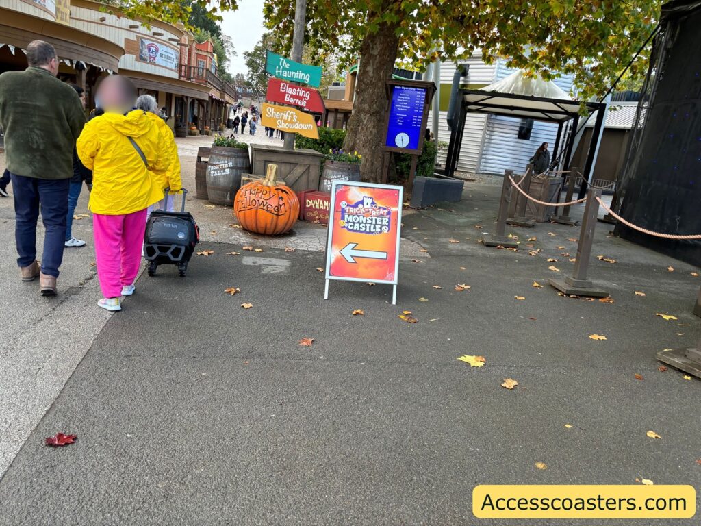 People, including a child carrying a trick-or-treat bucket, walking towards the entrance to the castle’s Halloween event, guided by clear signage and surrounded by pumpkins.