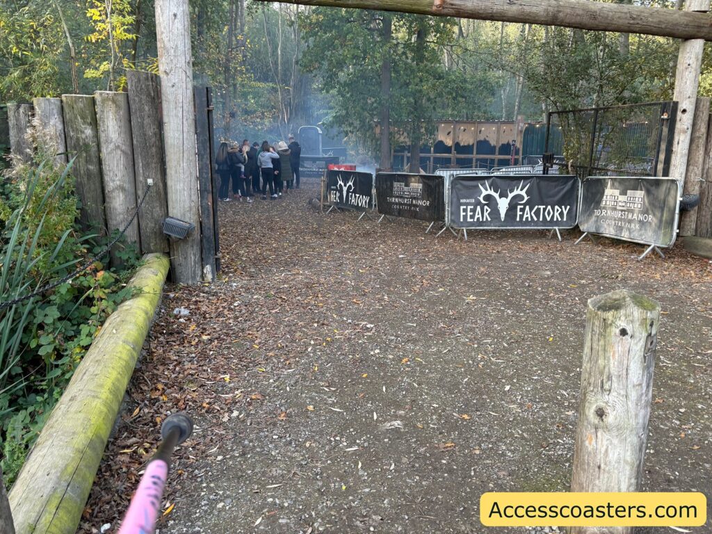 Wooden fenced entry path to Fear Factory, with people gathered and event banners on display.