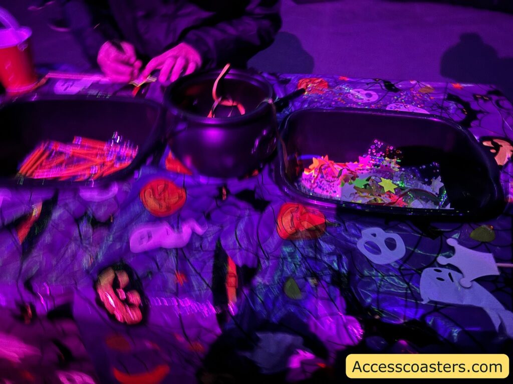 A table filled with craft supplies like glow-in-the-dark pens, colorful gems, and other materials for decorating magic wands.