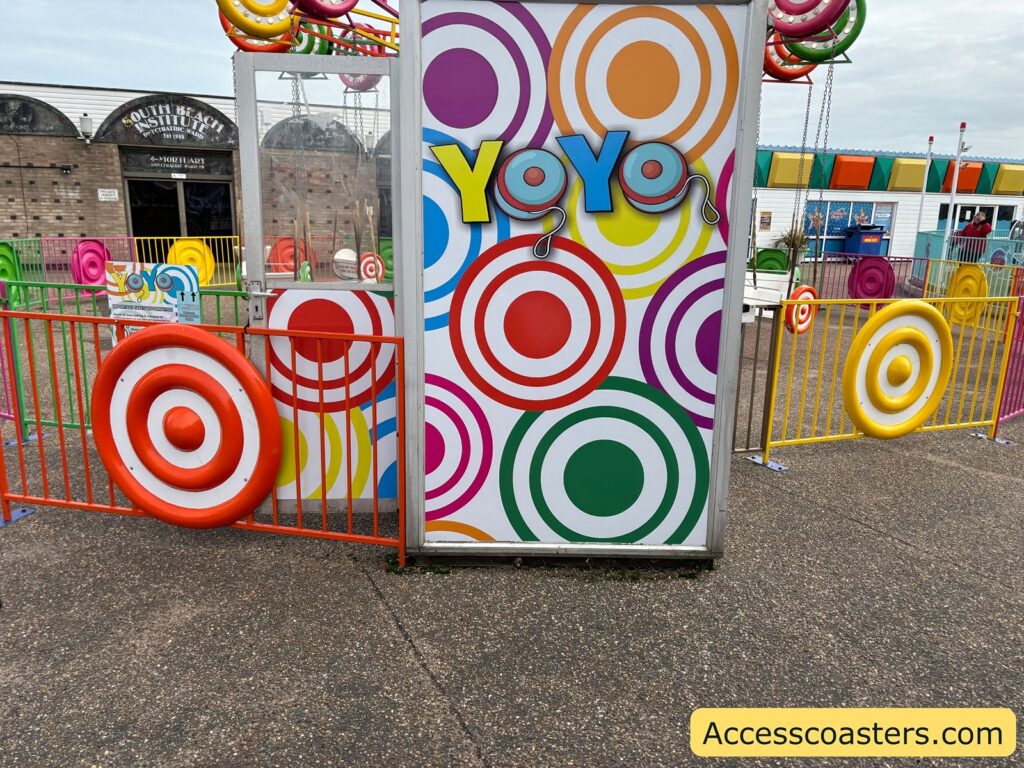 entrance to the Yo-Yo Ride at an amusement park, featuring a sign with the word "YOYO" and colorful circular patterns in red, orange, yellow, green, and purple. Brightly colored fences surround the area.