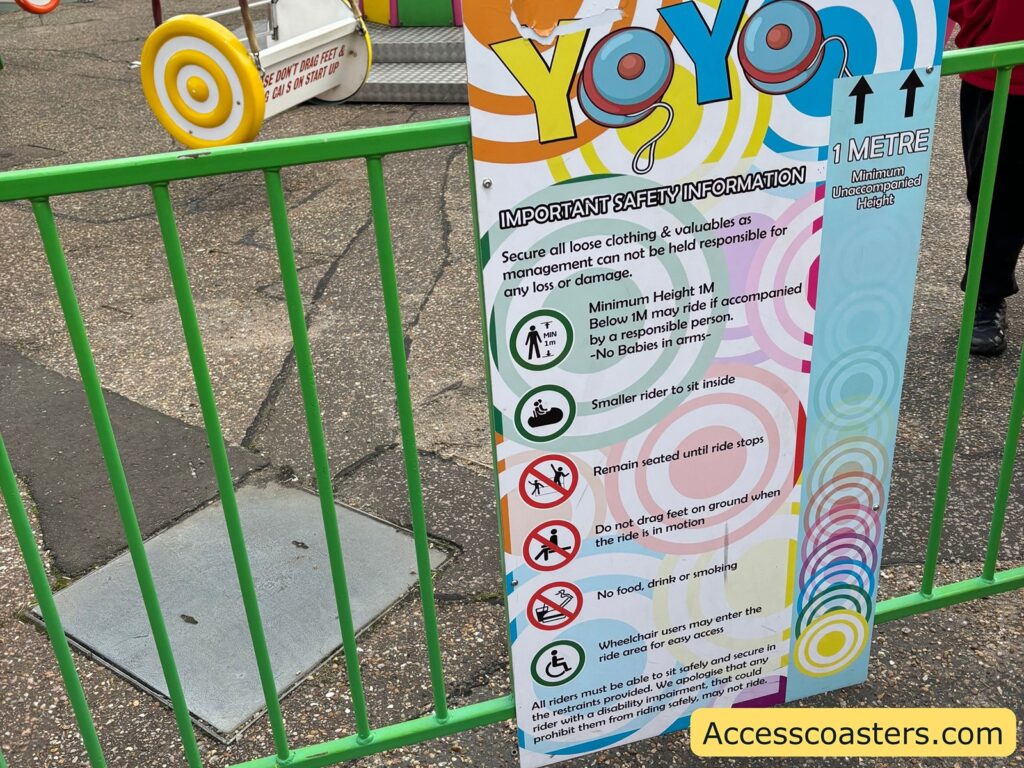 lose-up of the Yo-Yo Ride entrance signage, displaying ride rules and information, with a green fence and part of the ride visible in the background.