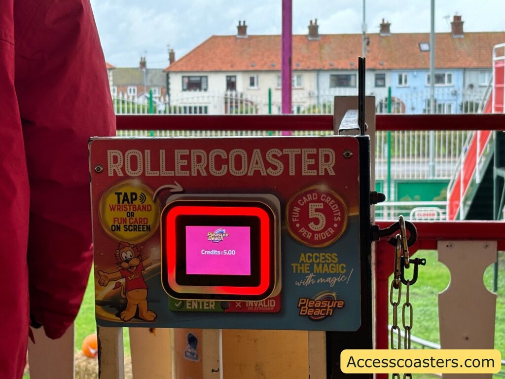 A close-up shows a ride access scanner with a pink display reading “credits: 5” located on the Rollercoaster ride. The scanner has instructions to tap your fun card or wristband on it.